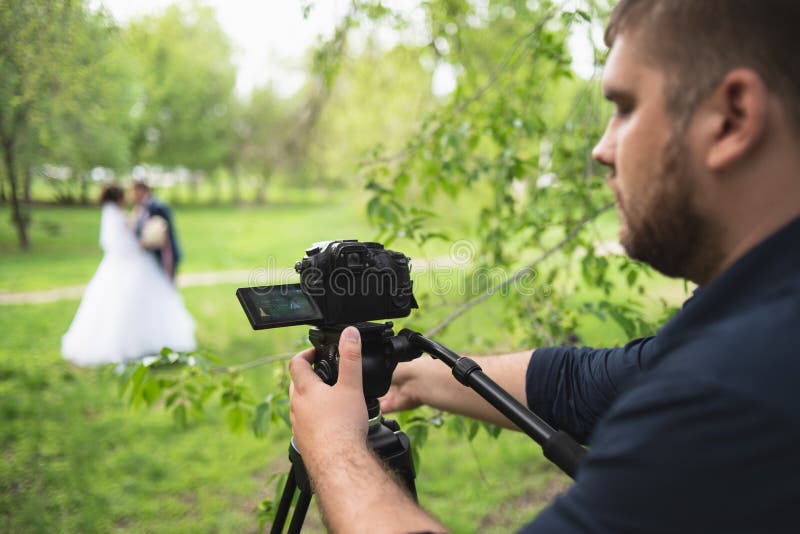 O videógrafo assina os casamentos no jardim no verão imagem de stock O videógrafo assina os casamentos no jardim no verão imagem de stock