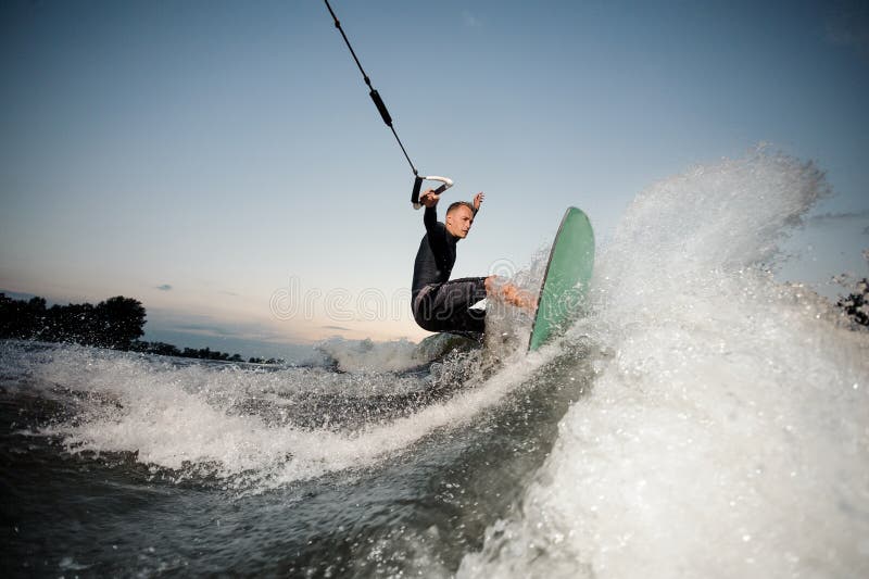 O wakesurfer ativo que monta abaixo das ondas azuis da elevação do rio com espirra imagem de stock O wakesurfer ativo que monta abaixo das ondas azuis da elevação do rio com espirra imagem de stock