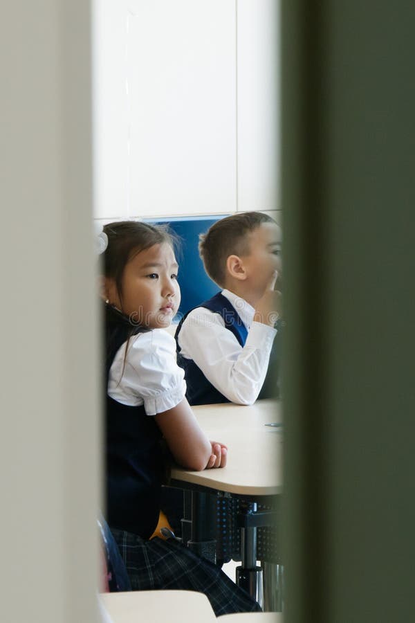 Tyumen, Russia, September 2, 2018. School. Half-open doors of classroom. It can be seen how girl and boy in school uniform sit at desk and attentively listen to teacher. Tyumen, Russia, September 2, 2018. School. Half-open doors of classroom. It can be seen how girl and boy in school uniform sit at desk and attentively listen to teacher