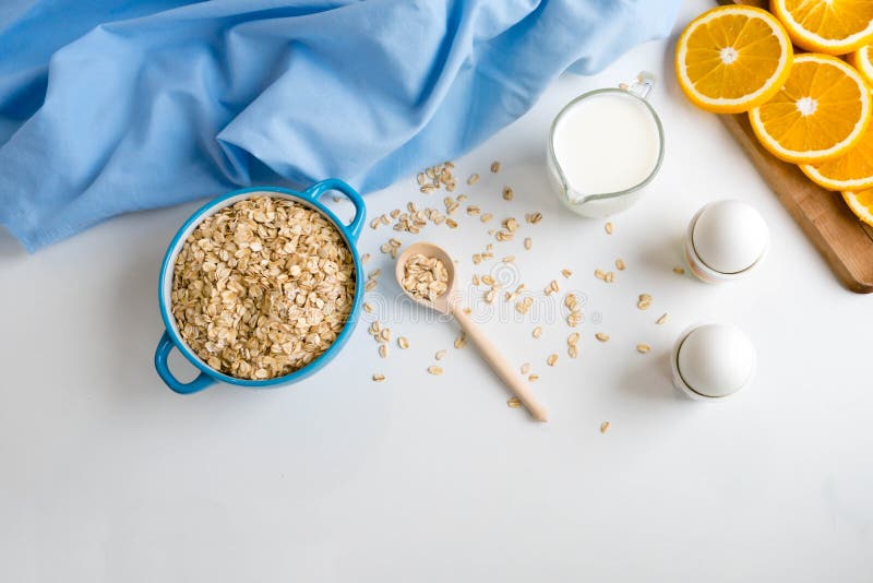 Oat flakes plate with milk, orange, eggs on a wooden white table. Top view of healthy oat flakes breakfast. Copy space. proteins a