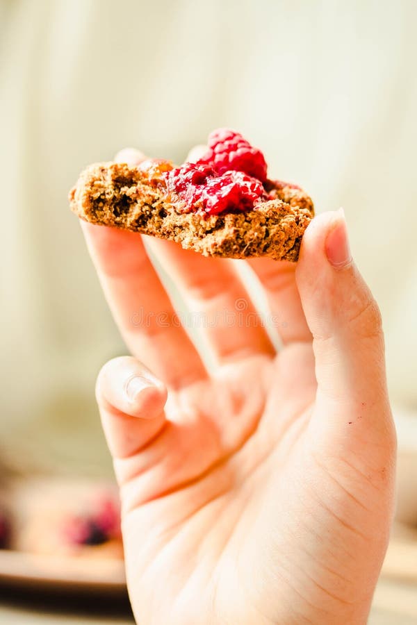 Oatmeal cookies with raspberry jam and date caramel in the hands of a young woman. The process of eating royalty free stock images Oatmeal cookies with raspberry jam and date caramel in the hands of a young woman. The process of eating royalty free stock images