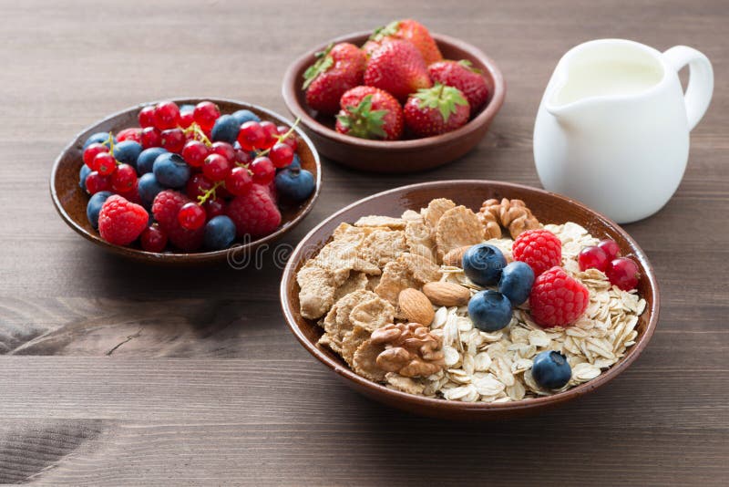 Oatmeal and muesli in a bowl, fresh berries and milk on wood