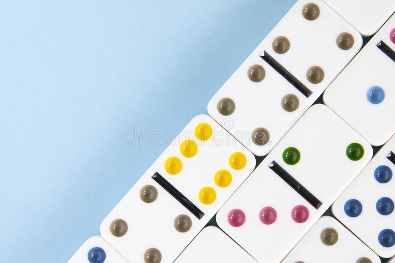 Obenliegende Nahaufnahme von weißen Dominos mit hell farbigen Punkten auf einem blauen Hintergrund mit Kopienraum