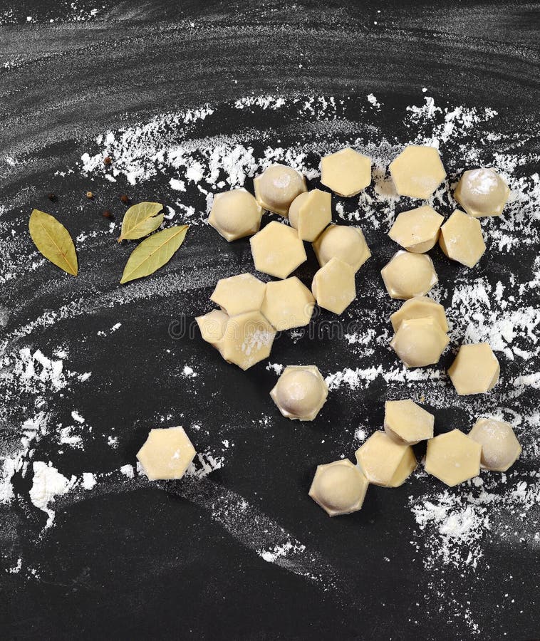 Oberedda dumplag, deg ravioli, på en svart baksida som är sprinklad med mjöl. arkivfoto