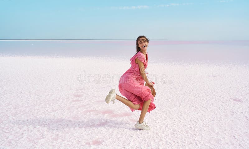 Obraz ruchu radosna śmieszna kobieta tańcząca w różowej sukience na plaży z słonym różowym jeziorem. fotografia stock