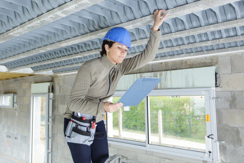 Obrera de la construcción en la escalera con el portapapeles inspeccionando el techo imágenes de archivo libres de regalías