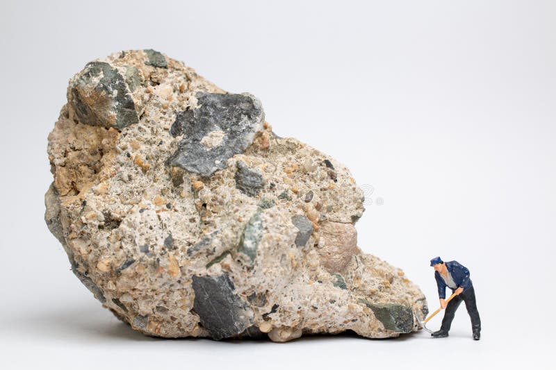 Obrero en miniatura que utiliza un pickaxe para patear en una roca grande sobre fondo blanco