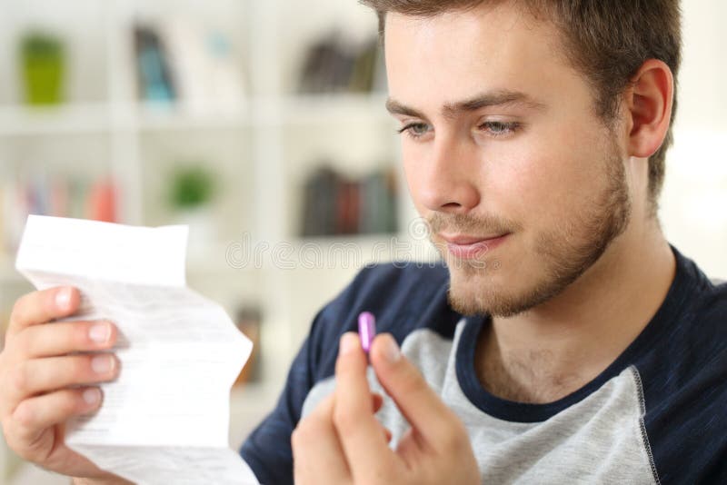 Man reading a leaflet before to take a pink pill sitting on a sofa in the living room in a house interior. Man reading a leaflet before to take a pink pill sitting on a sofa in the living room in a house interior