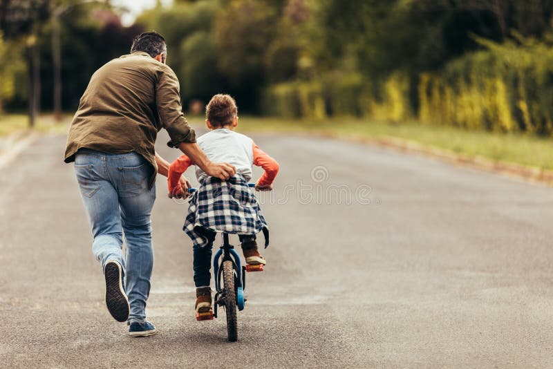 Obsługuje pomagać jego dzieciaka w uczenie jechać bicykl fotografia stock