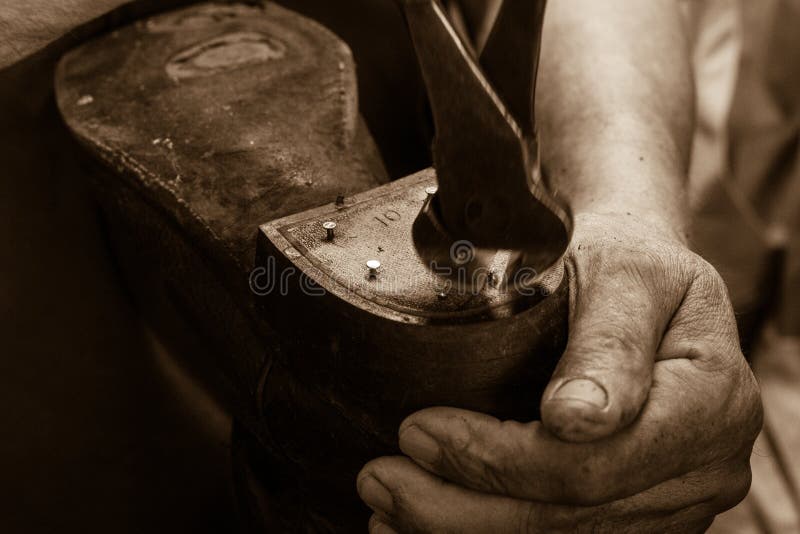 Closeup of cobbler working with old, worn tools to repair old, worn boot with strong, aged hands, in sepia. Closeup of cobbler working with old, worn tools to repair old, worn boot with strong, aged hands, in sepia