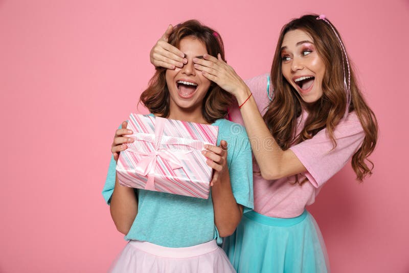 Occhi graziosi felici della copertura della giovane donna di sua sorella che dà regalo immagini stock Occhi graziosi felici della copertura della giovane donna di sua sorella che dà regalo immagini stock