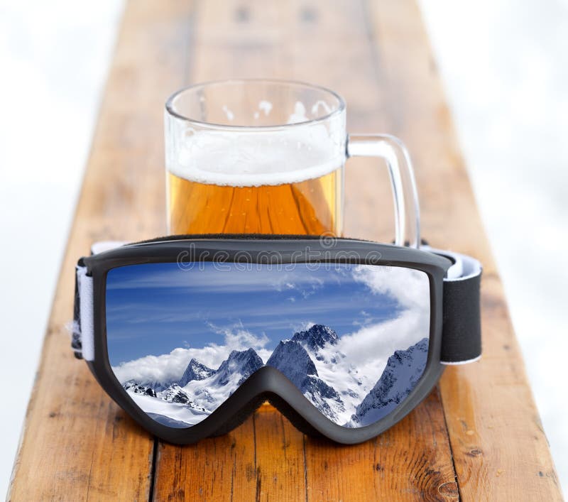 Occhiali di protezione dello sci con la riflessione della tazza di vetro e del montagna con birra fredda fresca fotografia stock libera da diritti Occhiali di protezione dello sci con la riflessione della tazza di vetro e del montagna con birra fredda fresca fotografia stock libera da diritti