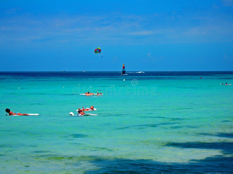 In the foreground swimmers float on water while sailing, parasailing and boating goes on in the background. In the foreground swimmers float on water while sailing, parasailing and boating goes on in the background