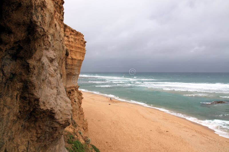 Scenic view of ocean cliff and snowy wave approaching the large sandy beach under cloudy sky. View from the Great Ocean Road. Scenic view of ocean cliff and snowy wave approaching the large sandy beach under cloudy sky. View from the Great Ocean Road.