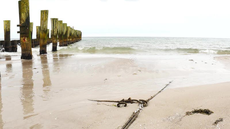 Ocean coast line with anchors rope and wooden poles on beach