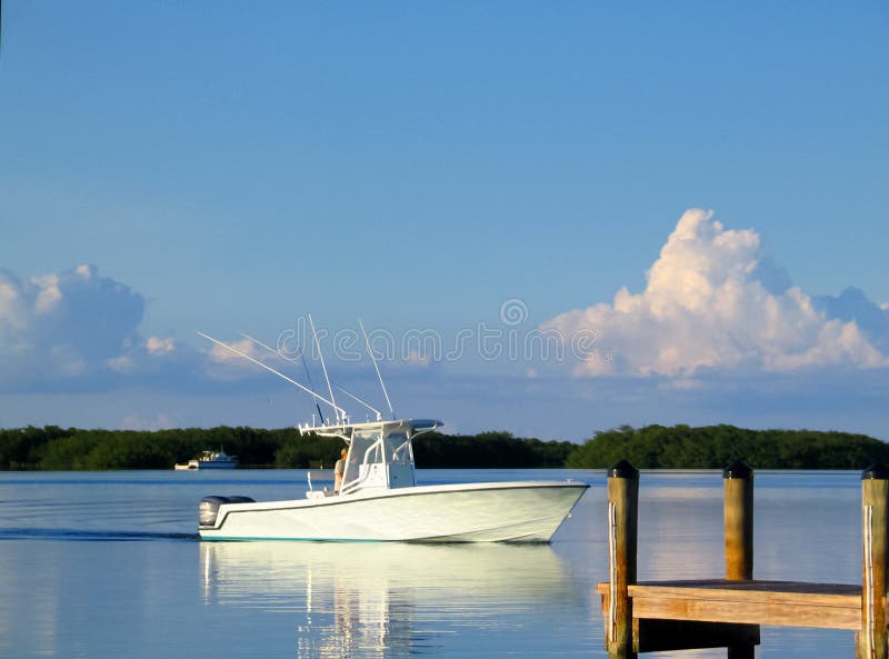 An Ocean Fishing Boat out on the bay nearing dock with reflection on calm water and beautiful clouds and sky