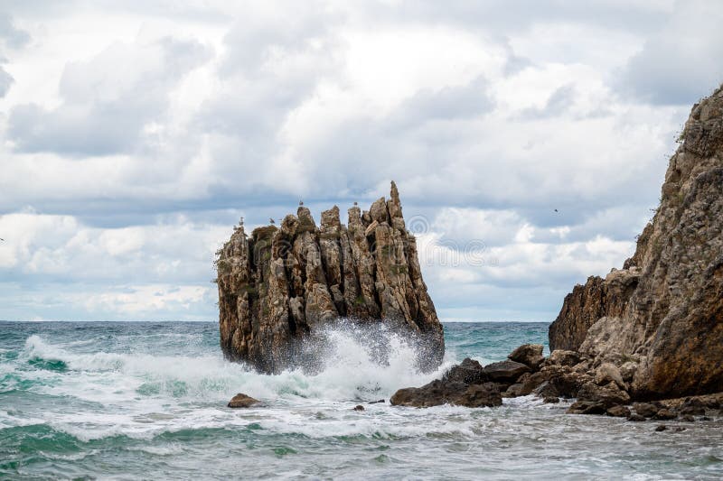 Ocean water splash on rock beach with beautiful sky and clouds. Sea wave splashing on stone at sea shore on winter. Sea waves lash