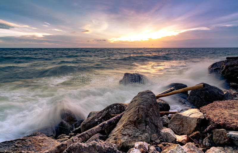 Ocean water splash on rock beach with beautiful sunset sky and clouds. Sea wave splashing on stone at sea shore on summer. Nature