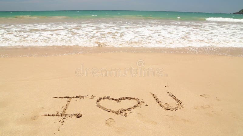 Ocean wave approaching words I love you written in sand on beach