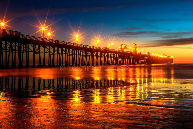 This image of a pier was captured in Oceanside, California not too long after sunset. The pier lights make nice reflections and the pilings are also reflected in the ocean water. This image of a pier was captured in Oceanside, California not too long after sunset. The pier lights make nice reflections and the pilings are also reflected in the ocean water.