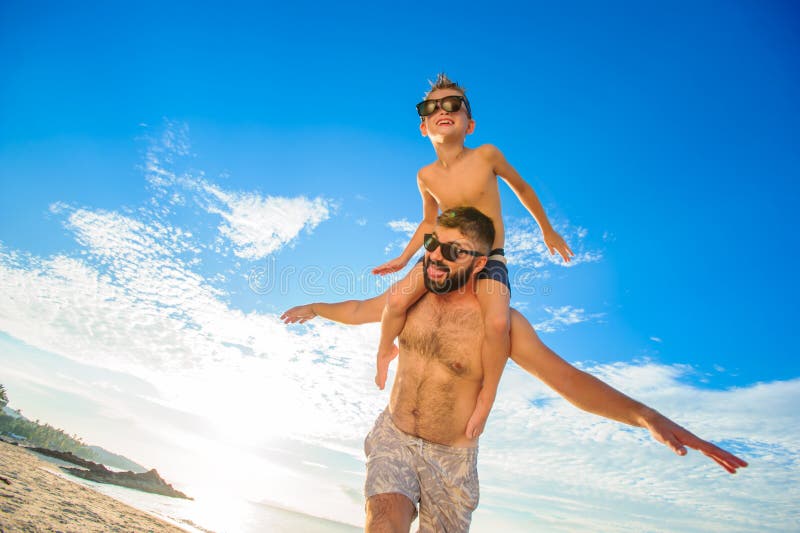 Ocho años del muchacho que se sienta en el ` s del papá llevan a hombros Ambos en pantalones cortos y gafas de sol de la natación imágenes de archivo libres de regalías Ocho años del muchacho que se sienta en el ` s del papá llevan a hombros Ambos en pantalones cortos y gafas de sol de la natación imágenes de archivo libres de regalías