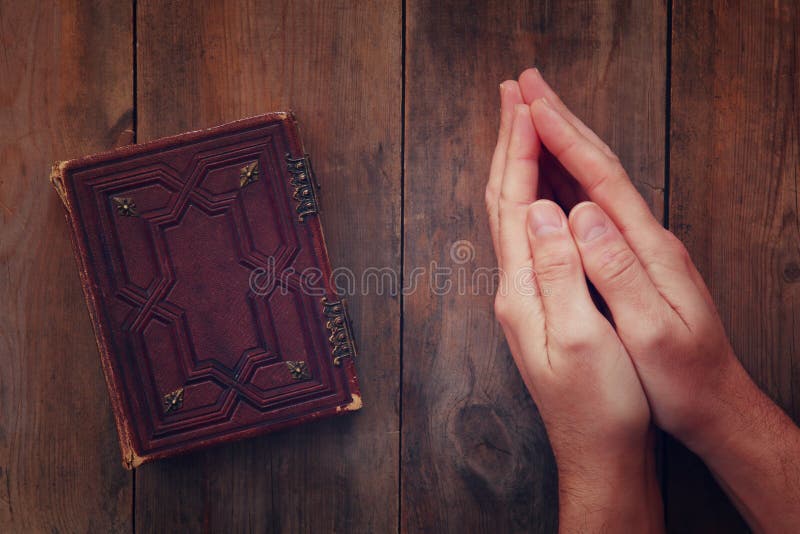 Top view image of mans hands folded in prayer next to prayer book. concept for religion, spirituality and faith. Top view image of mans hands folded in prayer next to prayer book. concept for religion, spirituality and faith.