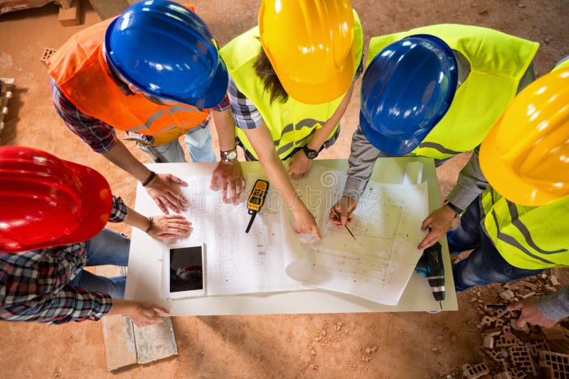 Top view of group of architects and engineers checking blue print if construction is going as planned. Top view of group of architects and engineers checking blue print if construction is going as planned