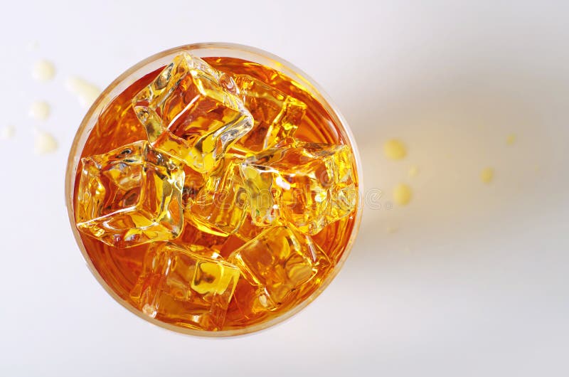 Top view on alcoholic drink in a glass with ice cubes and spilled drops on the table. Top view on alcoholic drink in a glass with ice cubes and spilled drops on the table