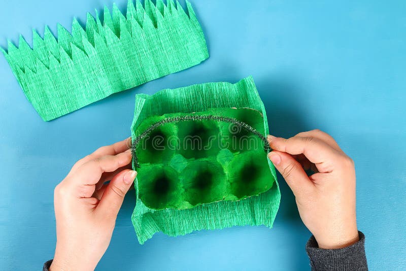 Oeuf de pâques de panier de DIY de plateau de carton, papier de crêpe, tige de chenille sur le fond bleu photos stock Oeuf de pâques de panier de DIY de plateau de carton, papier de crêpe, tige de chenille sur le fond bleu photos stock