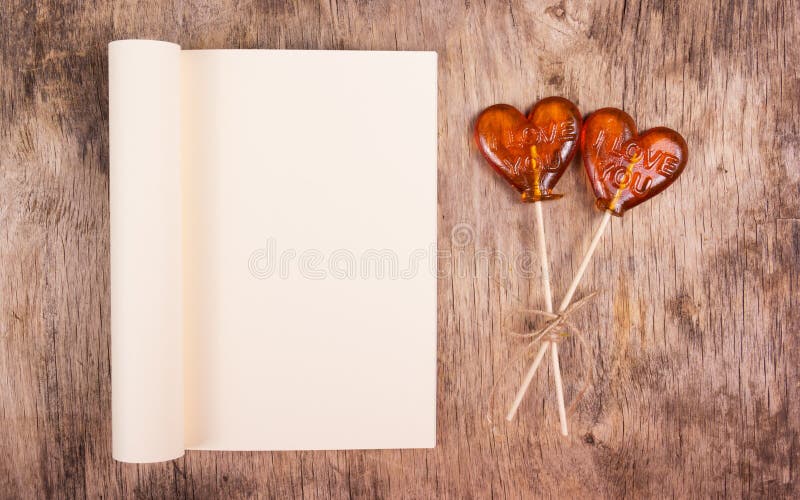Offenes Buch mit Leerseite und Lutscher zwei in Form eines Herzens auf einem alten Holztisch lizenzfreies stockbild Offenes Buch mit Leerseite und Lutscher zwei in Form eines Herzens auf einem alten Holztisch lizenzfreies stockbild