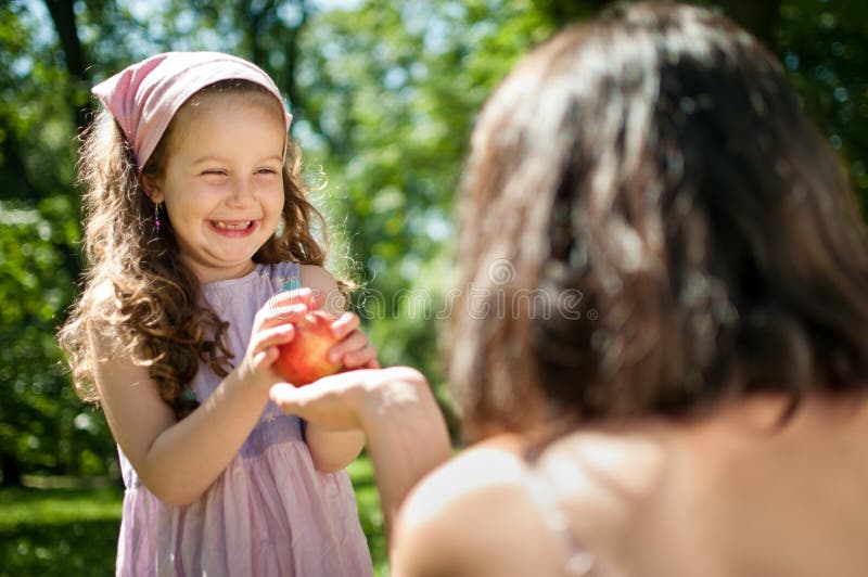 Offering apple - mother with child. Mother offering her smiling happy child apple - outdoor in nature stock photos Offering apple - mother with child. Mother offering her smiling happy child apple - outdoor in nature stock photos