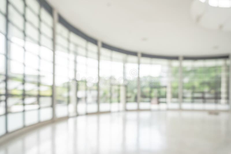 Office building or university lobby hall blur background with blurry school hallway corridor interior view toward empty corridor entrance, glass curtain wall, floor and exterior light illumination.