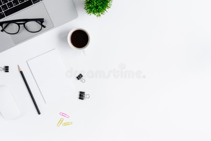 The office desk flat lay view with laptop, mouse, tree, pink and yellow paper clip, coffee cup, notebook, pencil, black glasses on