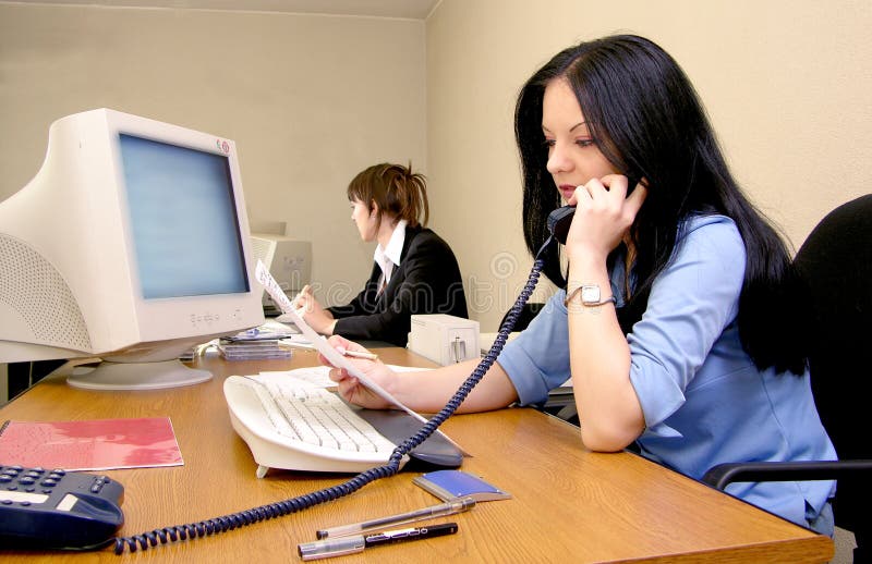 Dos mujer en negocios en oficina, uno en negocios sobre el computadora próximo discurso en teléfono.
