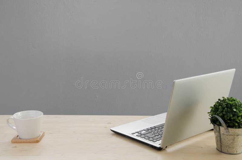 Office table with notebook, green tree on basket and white coffee cup. View from front with notebook space.