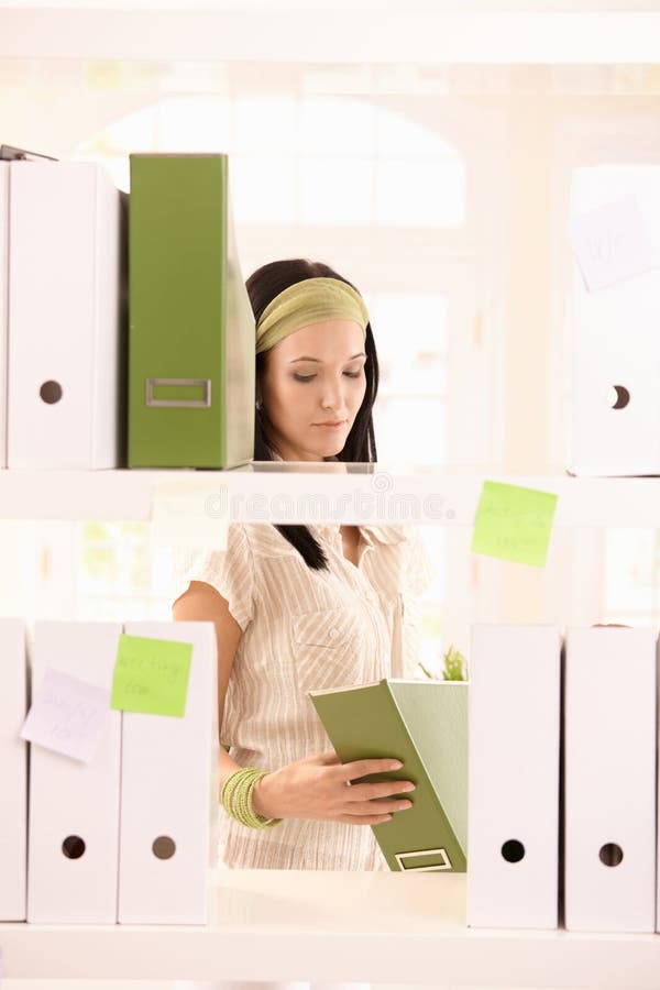 Pretty office worker girl packing folders on shelf. Standing file folder stock images, royalty-free photos and pictures