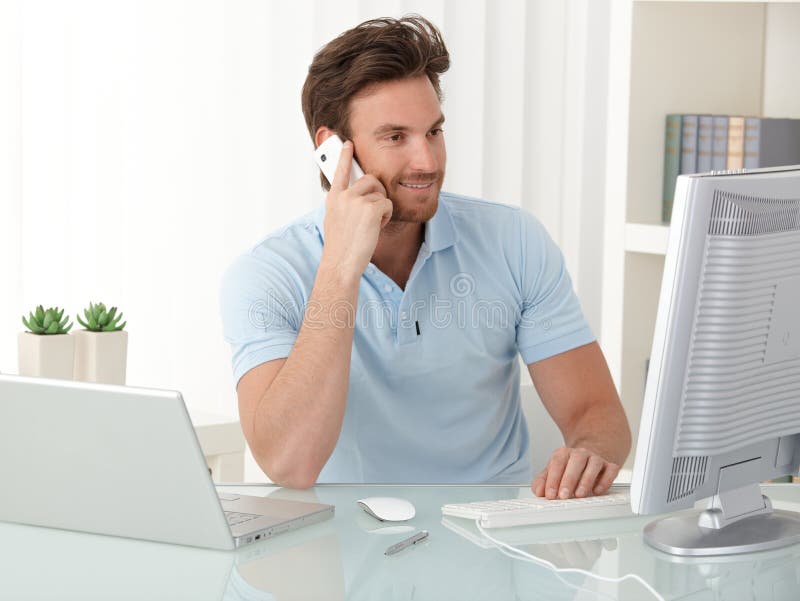 Administratívny pracovník, chlap na stôl pomocou stolného počítača, notebooku a mobilného telefónu pri práci, s úsmevom, pri pohľade na obrazovke.
