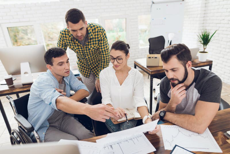Office workers and a person in a wheelchair discuss working matters. They work in a bright office. stock photo Office workers and a person in a wheelchair discuss working matters. They work in a bright office. stock photo