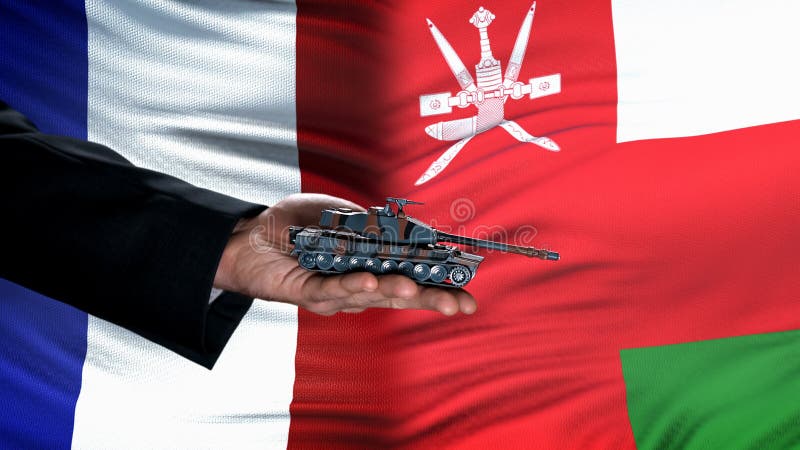Official hand holding toy tank against France and Oman flag background, army stock images
