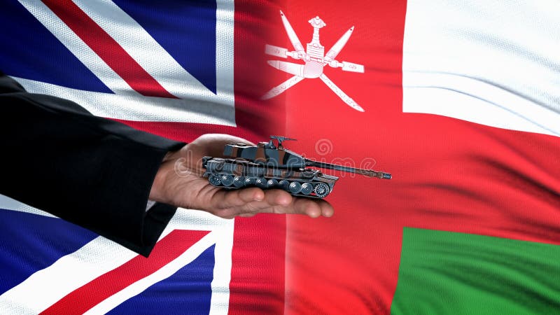 Official hand holding toy tank against Great Britain and Oman flag background royalty free stock image