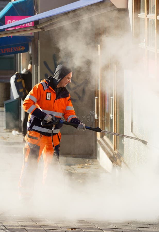 Official in orange uniform working to remove graffiti using steem on a wall in central Stockholm