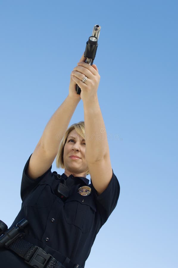 Low angle view of a female police officer aiming pistol against blue sky. Low angle view of a female police officer aiming pistol against blue sky