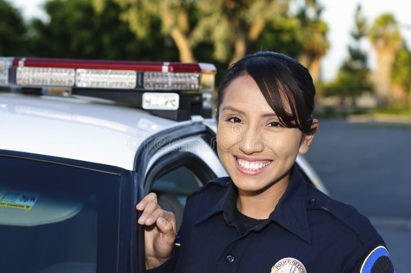 A Hispanic female police officer smiling and standing next to her unit. A Hispanic female police officer smiling and standing next to her unit.