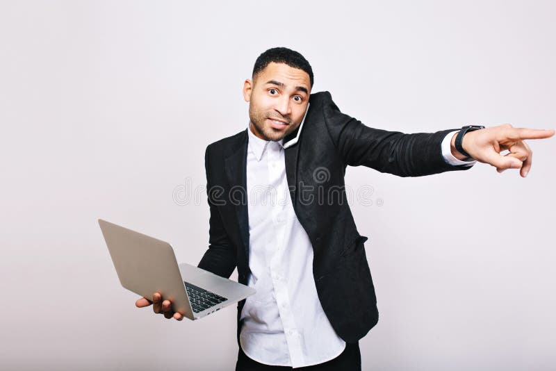 Oficinista hermoso alegre ocupado joven en la camisa blanca y el ordenador portátil negro de la tenencia de la chaqueta, hablando foto de archivo Oficinista hermoso alegre ocupado joven en la camisa blanca y el ordenador portátil negro de la tenencia de la chaqueta, hablando foto de archivo