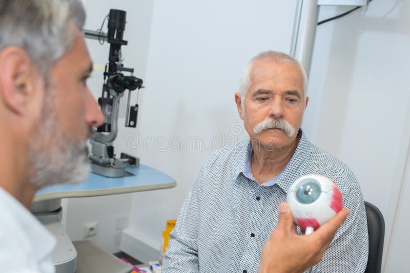 Oftalmólogo hermoso con el modelo del ojo en paciente delantero foto de archivo Oftalmólogo hermoso con el modelo del ojo en paciente delantero foto de archivo