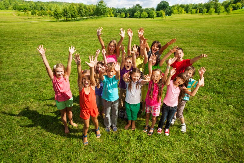 Large group of happy kids, boys and girls, about 10 years old with lifted hands smiling and screaming, standing on the green grass shoot from above. Large group of happy kids, boys and girls, about 10 years old with lifted hands smiling and screaming, standing on the green grass shoot from above