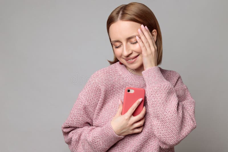 Oh so cute. Pleasant cheerful lovely european woman holding smartphone clasped to her chest and heart, closed eyes stock photos Oh so cute. Pleasant cheerful lovely european woman holding smartphone clasped to her chest and heart, closed eyes stock photos