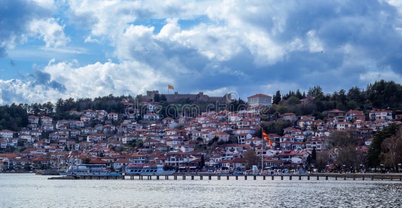 Panoramic view of Ohrid Old Town with traditional red-roofed houses cascading down to Lake Ohrid, surrounded by lush hills.