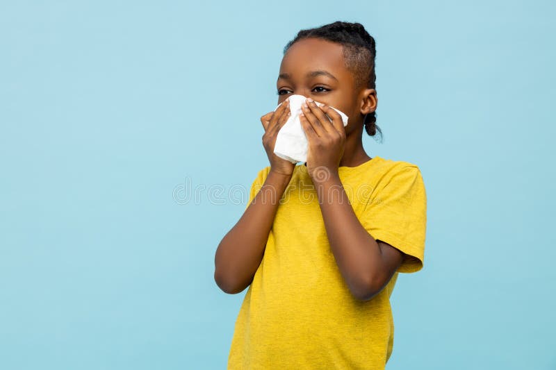 Unhealthy dark- skinned little boy suffering runny nose isolated over blue background. Unhealthy dark- skinned little boy suffering runny nose isolated over blue background