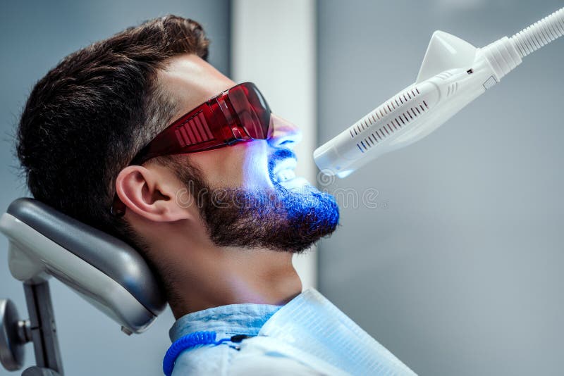 Oigenkännlig tandläkare som gör vit tänder av den unga mannen som sitter i tand- stol i modern klinik Slapp fokus royaltyfri foto Oigenkännlig tandläkare som gör vit tänder av den unga mannen som sitter i tand- stol i modern klinik Slapp fokus royaltyfri foto